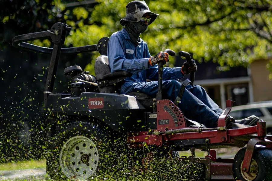 Greenline crew member operating a zero-turn mower on a residential lawn, grass clippings flying