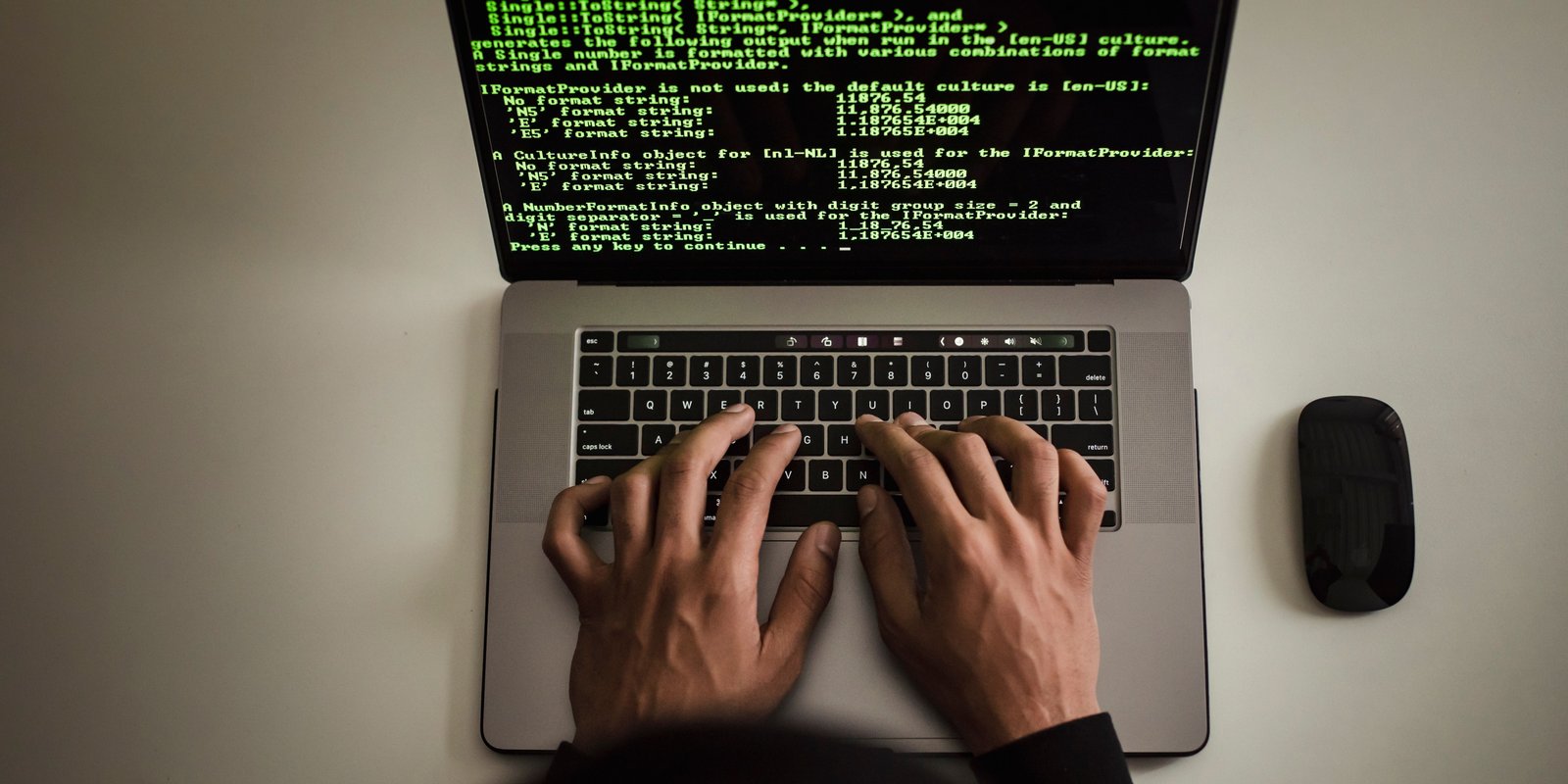 Overhead view of hands typing on a laptop, its screen filled with green code on a black background.